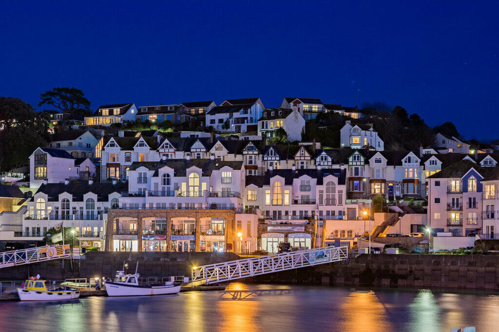 Brixham Harbour at night, lit up by street lights and lights from the houses.